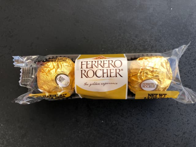 Коробка Ferrero Rocher с тремя развёрнутыми конфетами в золотой фольге на гофрированных бумажных подставках