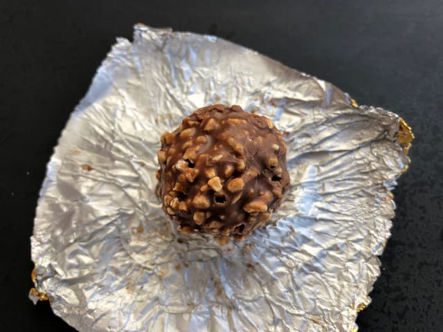 Развёрнутая конфета Ferrero Rocher без фольги, лежит на бумажной подложке
