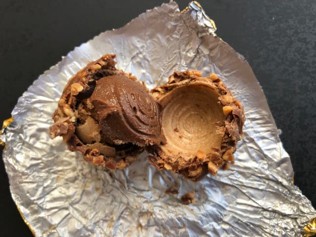 Конфета Ferrero Rocher, разломанная пополам — видна структура: орех в центре, вафля, ореховый крем и шоколадное покрытие